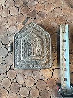 front view of metal amulet box with ruler for scale