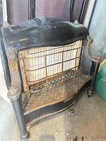 Front view of black cast iron antique fireplace insert showing ornate columns, wire guard and perforated hearth