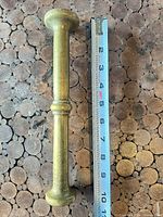 Full view brass pestle beside tape measure showing length