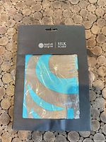 Front view of packaged tan and turquoise silk scarf