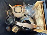 Overview of assorted teapots, kettle, French press, stainless containers, bamboo mat in bin