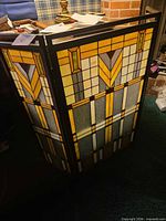 Front angled view of tri-fold stained glass look fireplace screen showing geometric design and metal frame