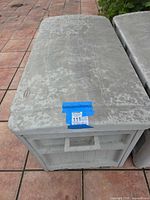 Top and front view of grey Suncast resin deck storage box with blue lot label