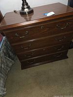 Front view of wood cabinet showing faux four-drawer front, two large drawers, brass-tone handles, keyhole