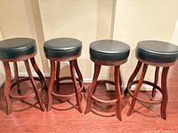 Front view of four wood bar stools with black leather seats