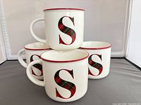 Stacked view of four matching mugs showing plaid S and red rim