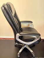 Side view of black faux leather executive chair showing padded backrest, seat, armrest and silver swivel base