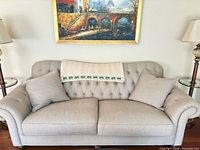 Front view of beige tufted 2-seat sofa with two pillows and artwork above