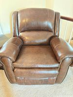 Front view of chestnut leather power recliner showing seating surface, arms, and nailhead trim