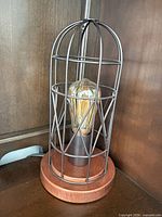 Front view of one lamp showing metal cage, wood base, Edison bulb