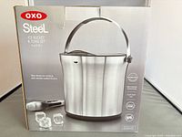 Front of retail box showing OXO Steel ice bucket, tongs, capacity 4 qt