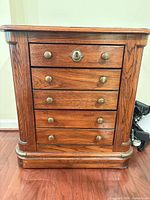 Front view showing five drawers, brass knobs, keyhole escutcheon, rounded corners, warm oak finish