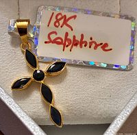 Front view of 18K yellow gold cross pendant with dark blue sapphires and tag