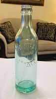 Full view of embossed green glass soda bottle front and neck