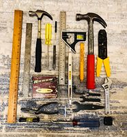 All items laid out on rug: rulers, hammers, screwdrivers, pliers, level, staple box, wrenches, hex keys