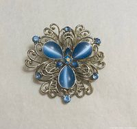 front view showing blue cat’s eye cabochons, rhinestones and filigree design