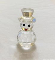 Front view of faceted clear crystal snowman figurine showing eyes, red nose-mouth, and top hat