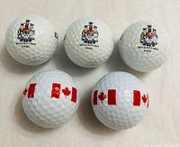 Five golf balls arranged, three with crest, two with Canadian flag design