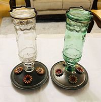 Pair of clear and green glass hummingbird feeders on metal bases