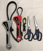 All three strap wrenches and two pairs of scissors laid out on white background