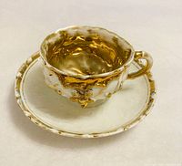 Cup on saucer showing gold interior and ornate exterior gilding