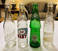 Front view of four vintage soda bottles showing logos and glass color/design