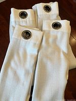 Four folded cream drapery panels showing grommets