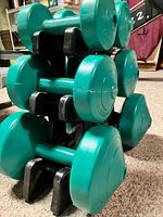 Stacked view of all six green dumbbells on black rack