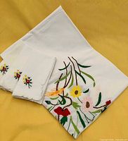 Folded tablecloth with main floral embroidery and three napkins showing corner motifs