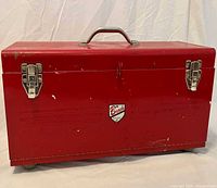 Front view of closed red toolbox showing latches, handle, brand badge and caster wheels
