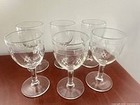 Group of six clear etched wine glasses on wooden surface