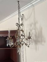 Full view of chandelier hanging from chain showing three arms, finish and crystal drops