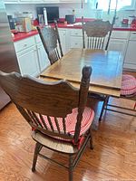 Table with extension leaf inserted, three of four matching carved chairs visible, red gingham cushions