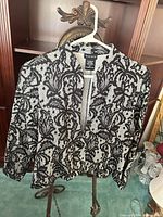 Front view of black and white floral lace jacket on hanger