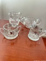 Four of the five clear pressed glass pieces showing floral patterns and handles
