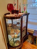 Three-quarter view of walnut display cabinet showing curved glass sides and contents