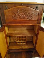 cabinet with lower doors open showing interior shelf and bottle grid, carved grape panel visible
