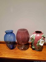 Three vases: blue blown glass, mauve footed glass, pink ceramic with calla lily relief