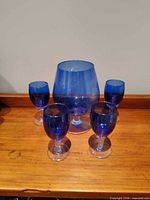 Large blue glass snifter and four small matching glasses on wood surface