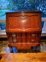Front view of closed desk showing sloped drop-front door, drawers, cabriole legs, brass hardware