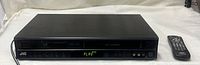 Front view of JVC HR-XVC11 player with remote, display lit