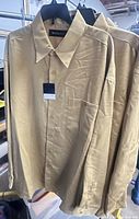 Front view of three beige Marquis shirts on hangers with tags