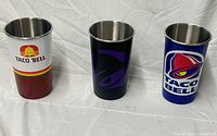 Front view of three Taco Bell stainless steel cups showing different logo designs