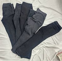 Six pairs of black denim jeans displayed on fabric