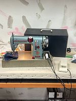 Front view of Sewmor 606 sewing machine on base with case behind, foot pedal and cord visible
