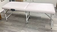 Top view of unfolded white massage table showing full length, vinyl surface and metal legs