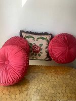 Group shot of three round satin pillows and one square needlepoint pillow