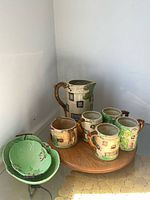 Group shot showing pitcher, five of six cups, creamer, two green leaf plates