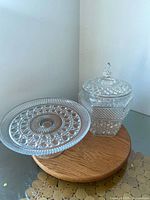 Pedestal cake stand beside lidded jar on wood riser