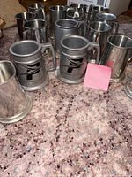 Group of pewter steins on carpet, mix of polished and matte with emblem